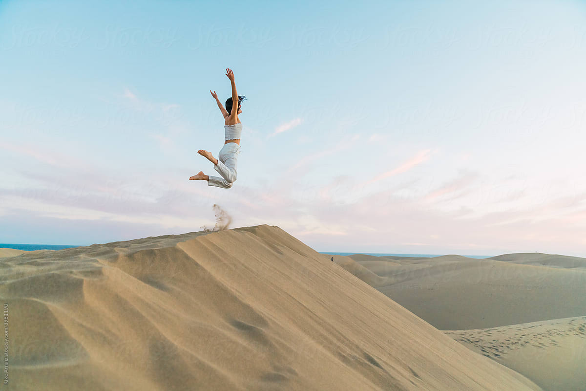 Woman standing and jumping on sand land and blue sky at sunset