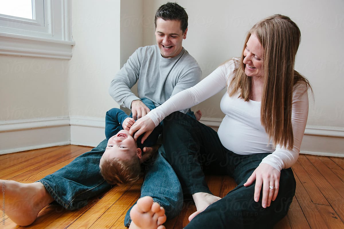 Pregnant mother and father tickle son sitting on floor