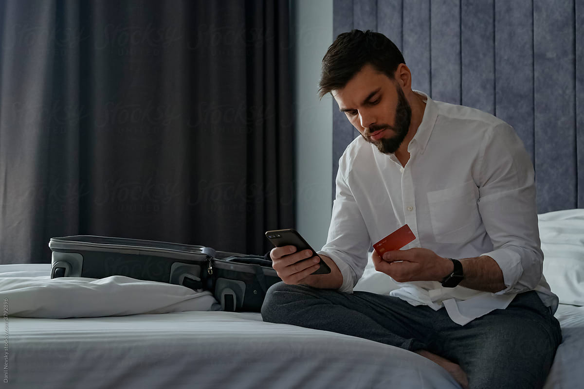 Focused man making online purchases via smartphone on bed