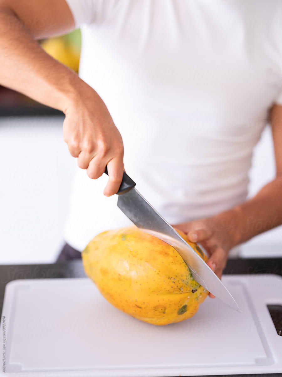 An apple is being sliced up on a white chopping board in a kitchen by a man.
