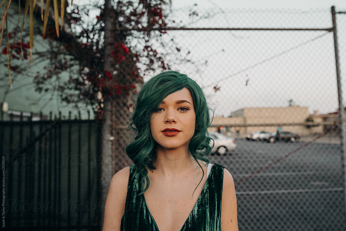 Young glamorous woman with green hair and red lipstick looking at the camera with a blank face