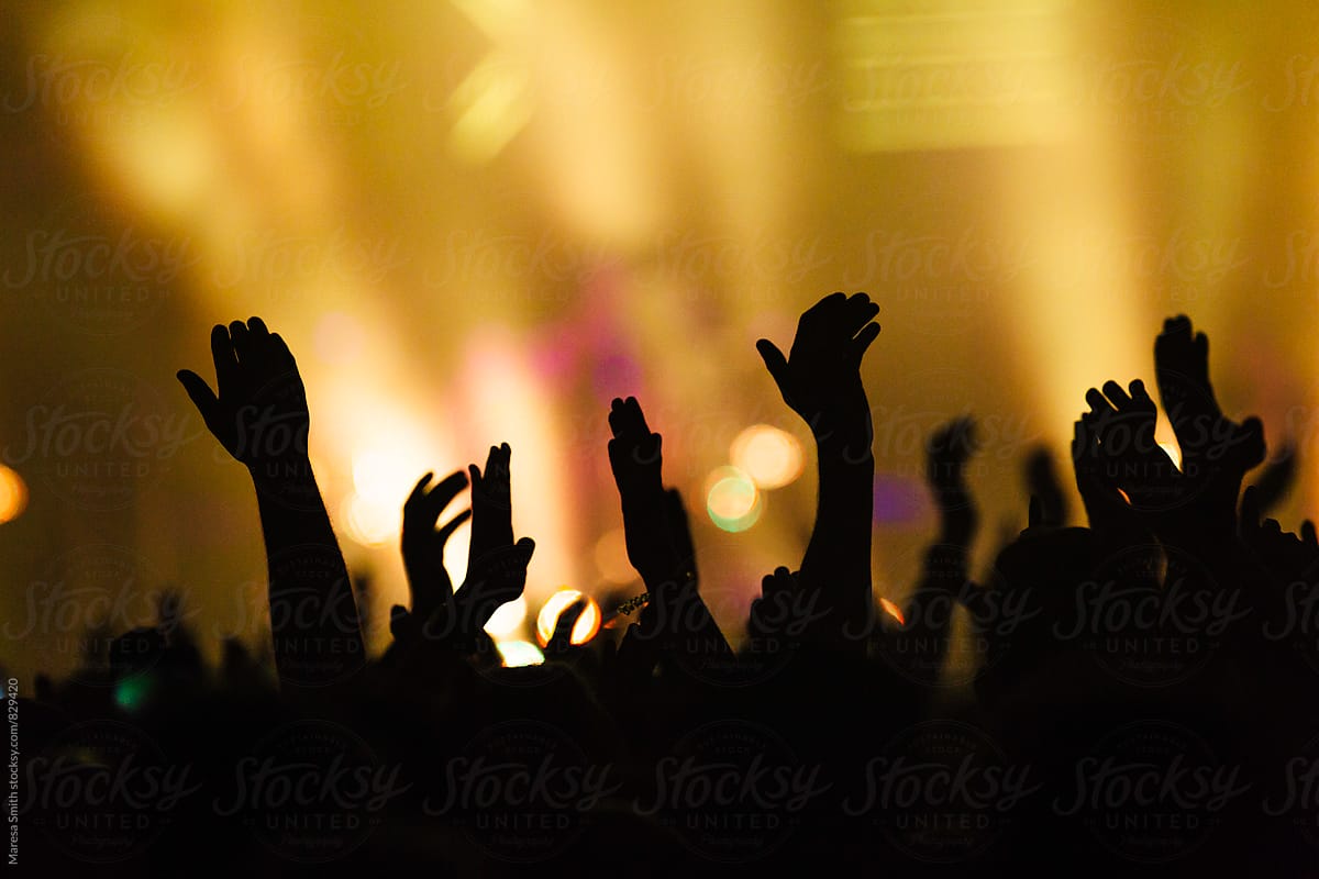 Hands in the air waving and clapping at a colourful concert