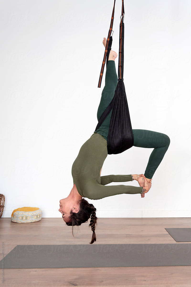 Flexible woman doing aerial yoga exercise on ropes