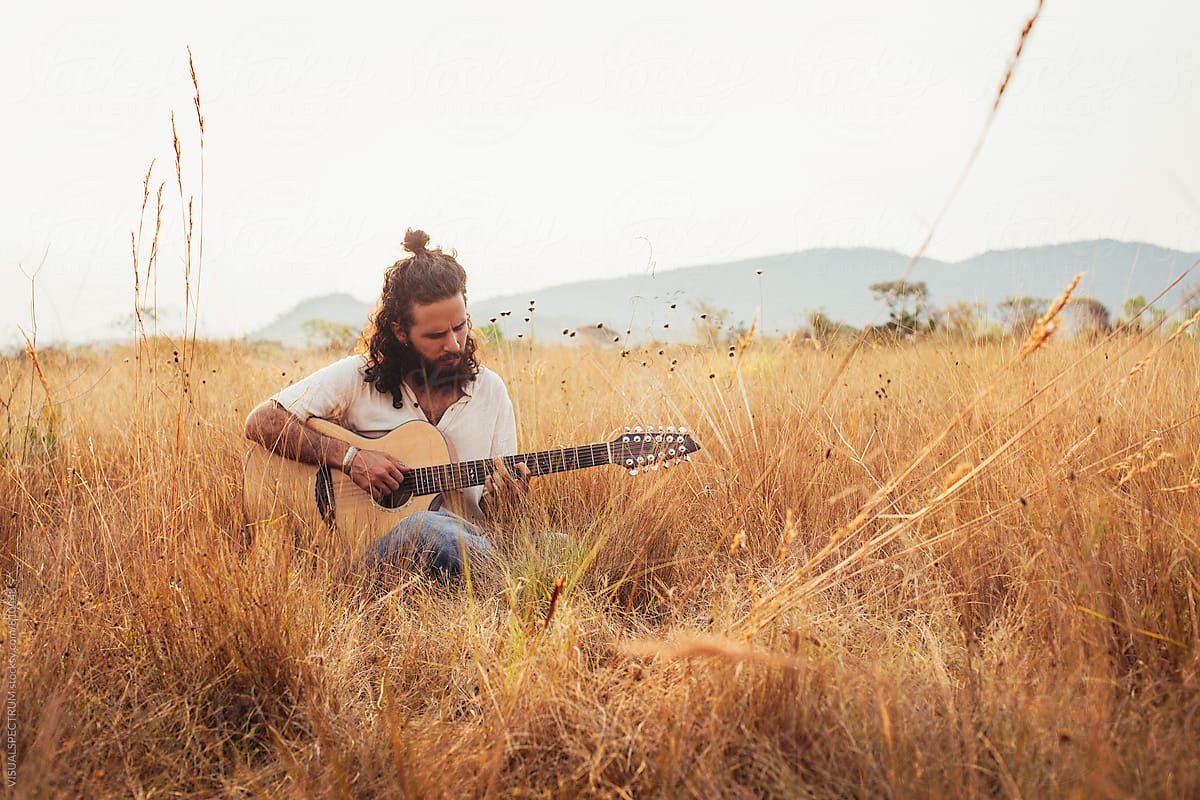 Bearded Young Male Musician Playing Guitar in Dry Grassland