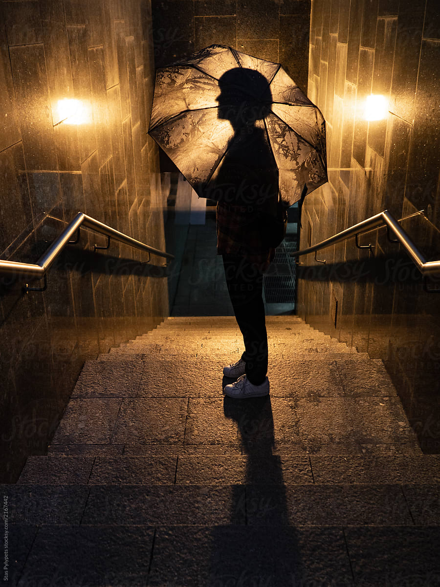 Silhouetted person with an umbrella at night in a big city