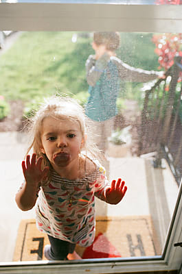 Little Girl Looks Through Front Door Screen by Stocksy