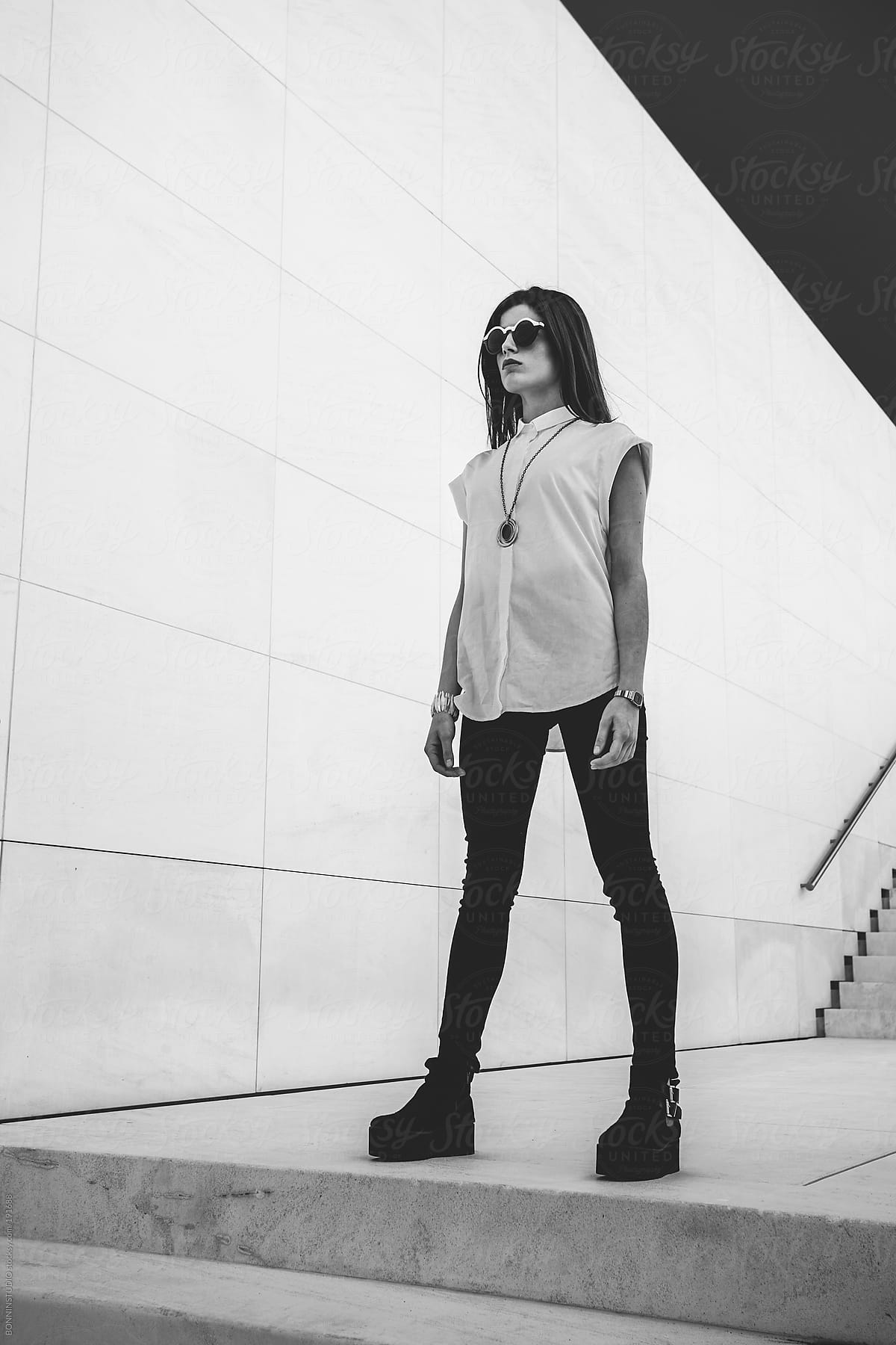 Young fashion woman with round sunglasses standing on white stairs.