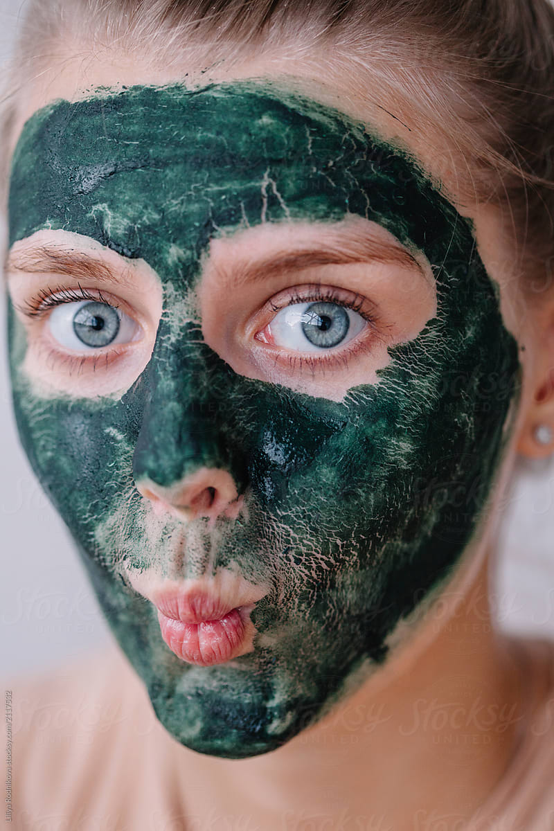 Lovely blue eyes girl having fun while using green mask for her skin