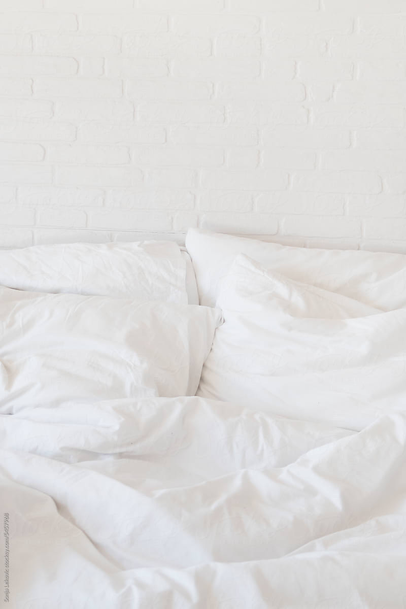 white bed sheets and pillows and white brick wall