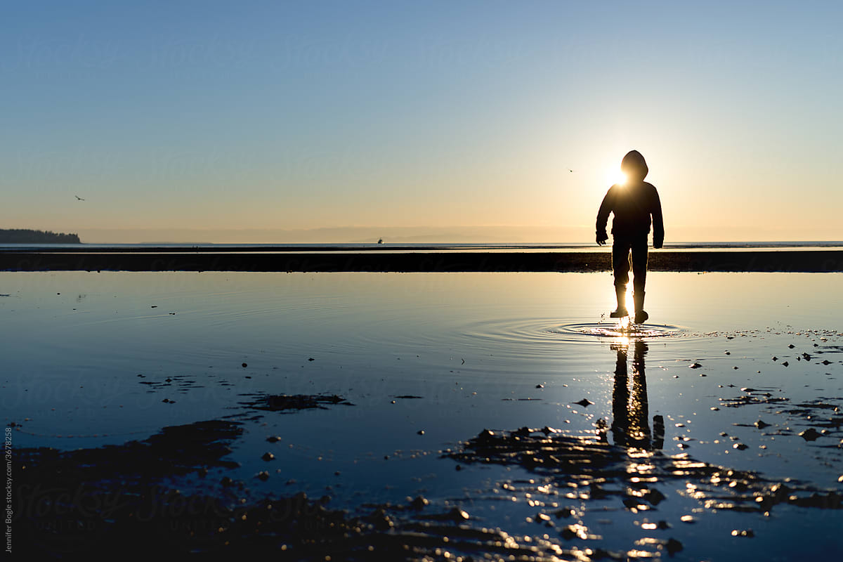 Silhouetted boy jumps in shallow tidepool