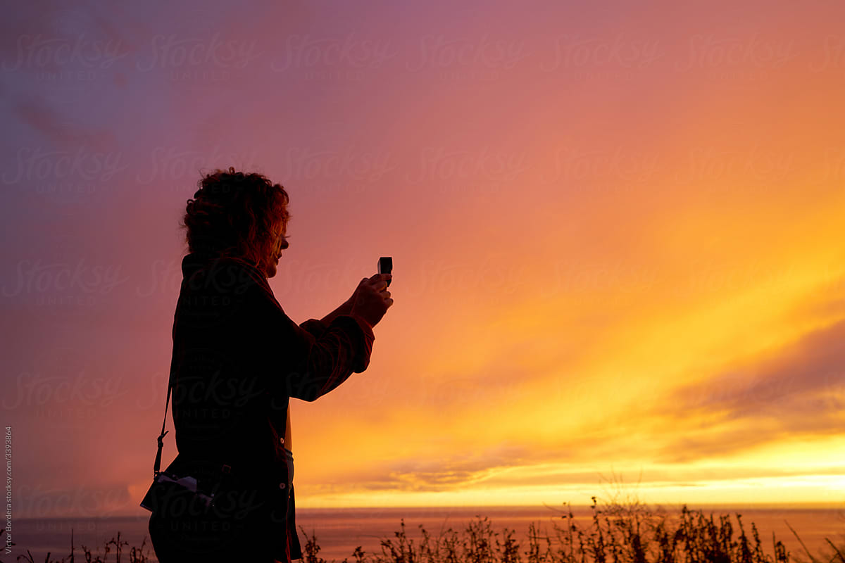 Wanderlust woman filming a sunset video with an action camera .