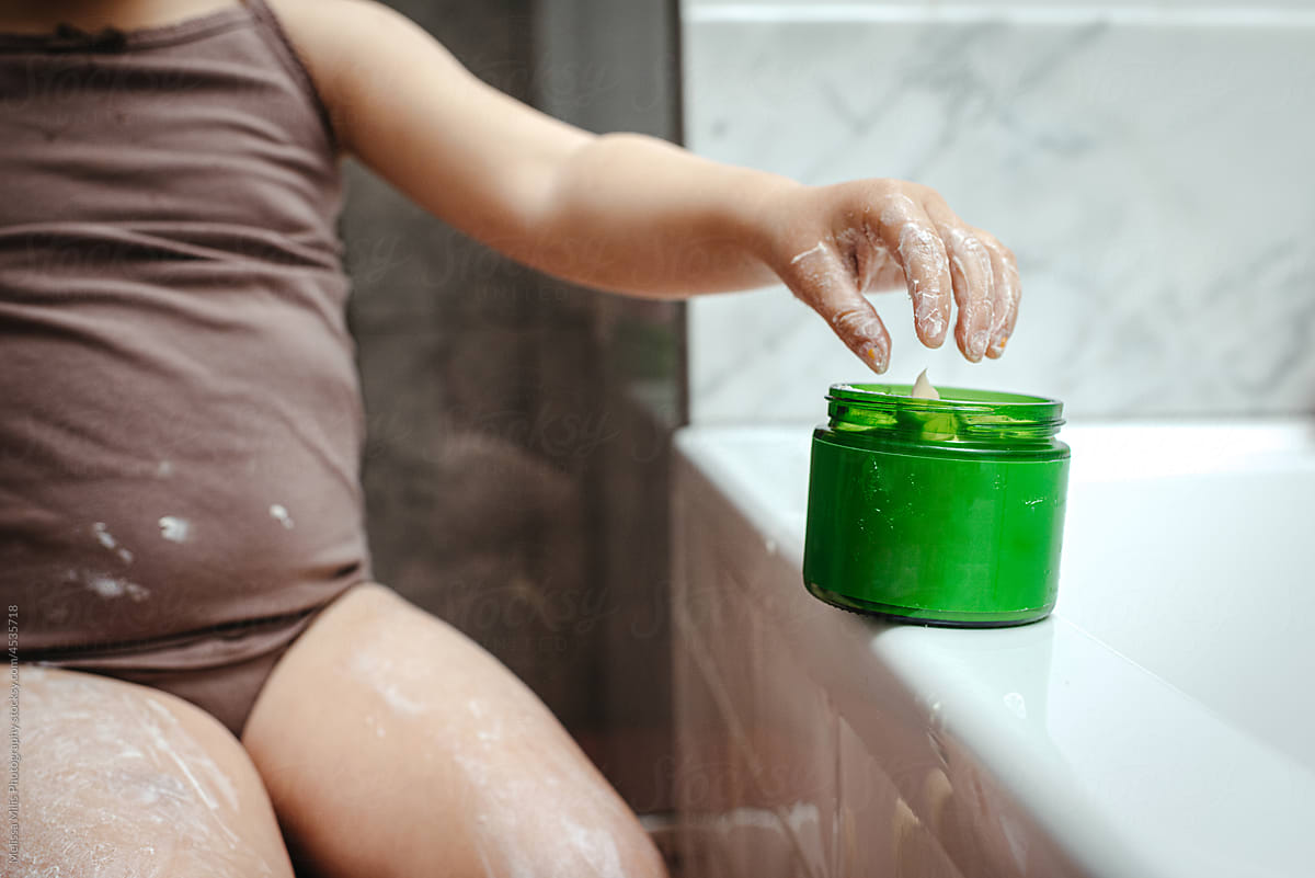 Close up of young girls hand taking body butter out of green cup