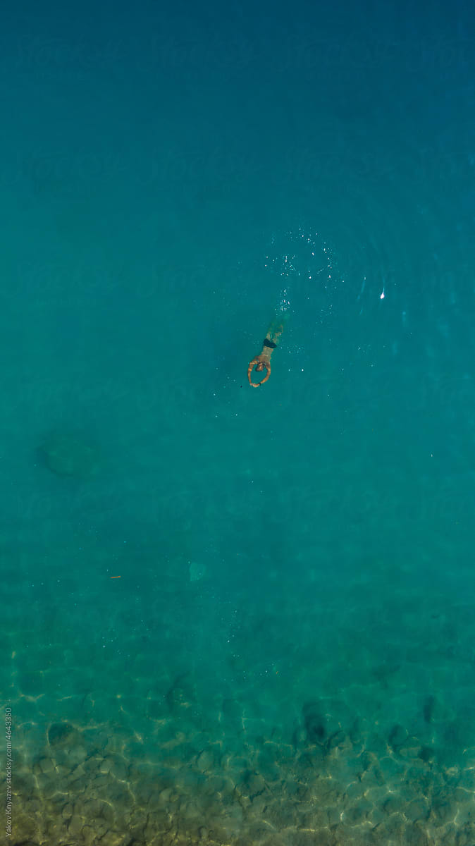 young man free diving in turquoise water by the coast