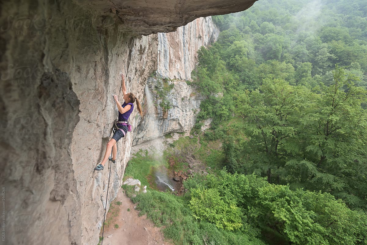 Side view of female rock climber ascending on rock wall