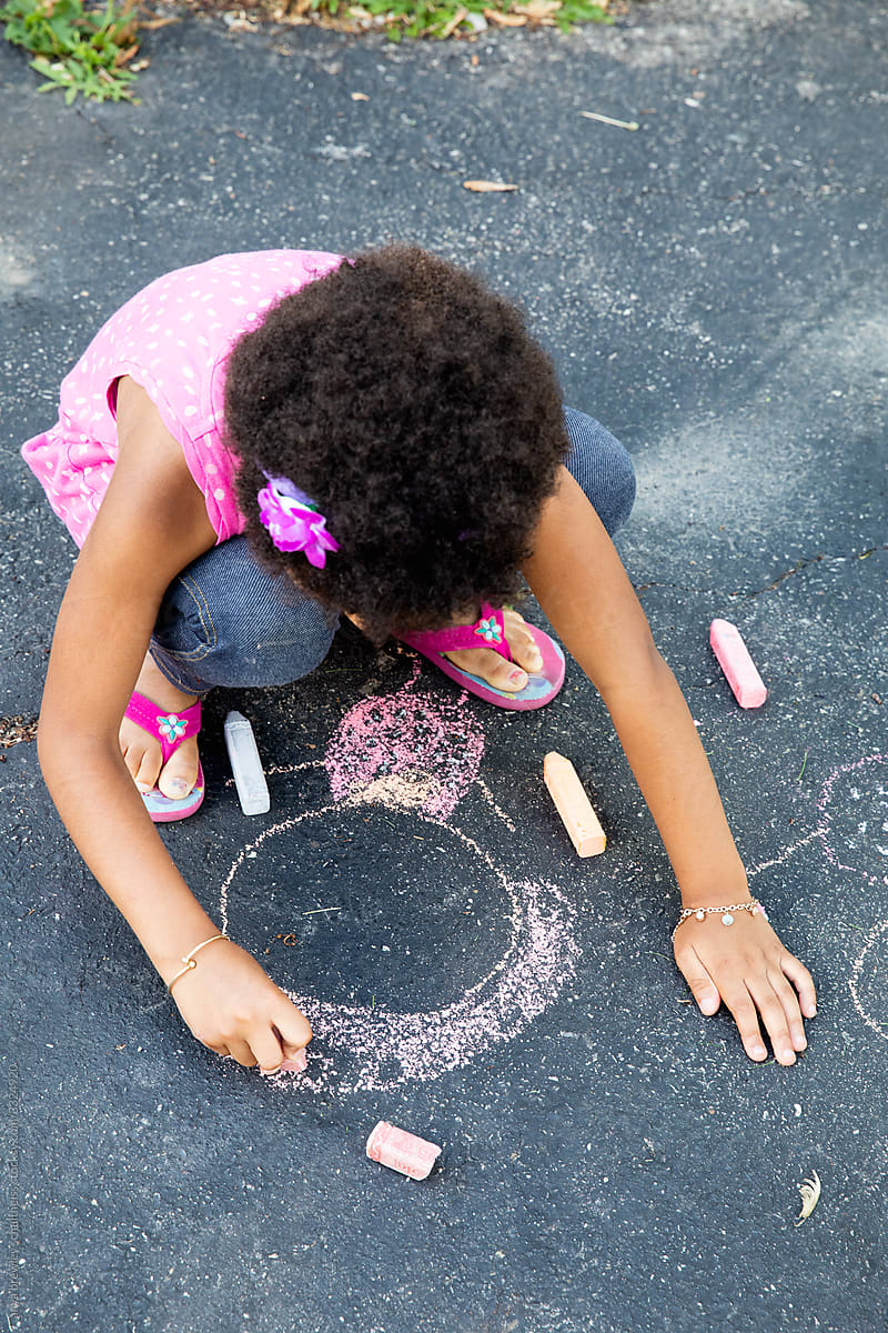 Curly haired girl drawing on the pavement with chalk