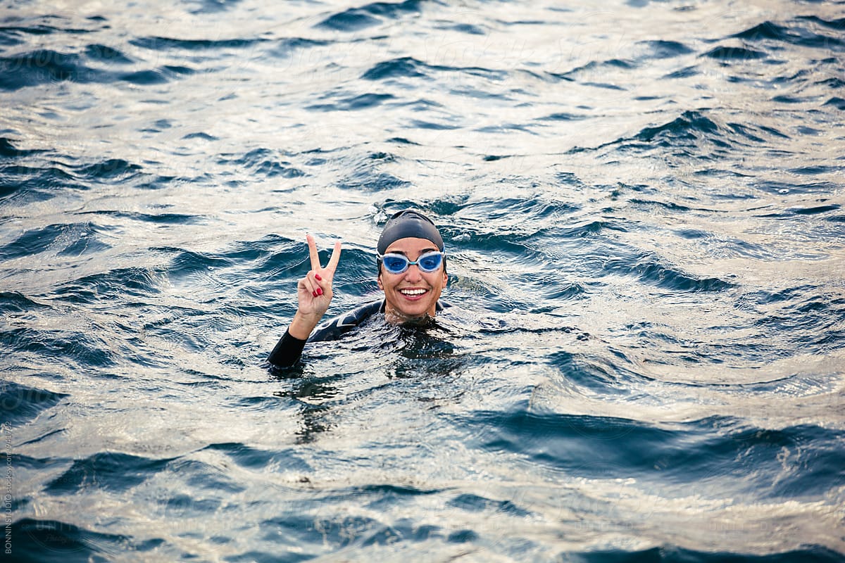 Smiling woman doing victory sign in the sea.