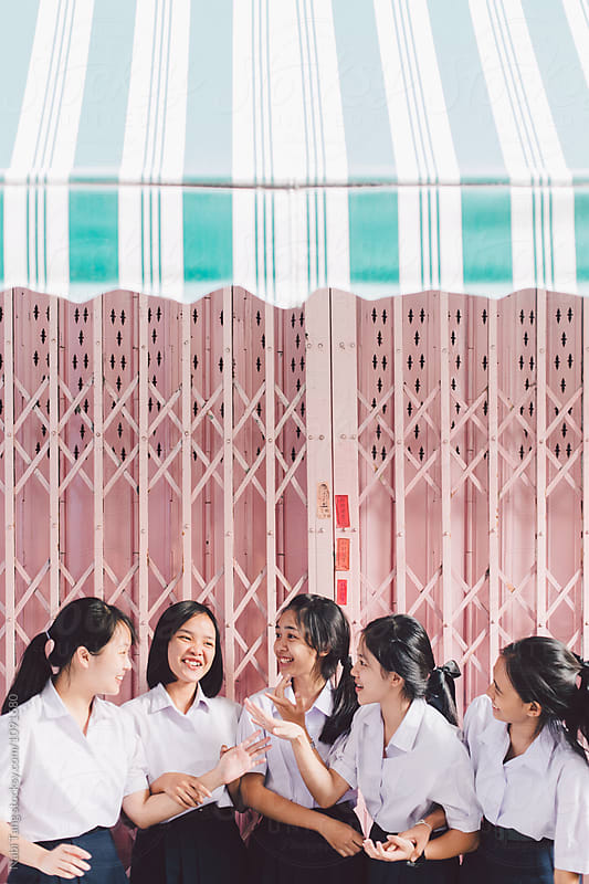 Asian high school girls standing in front of pastel pink garage door in Thailand