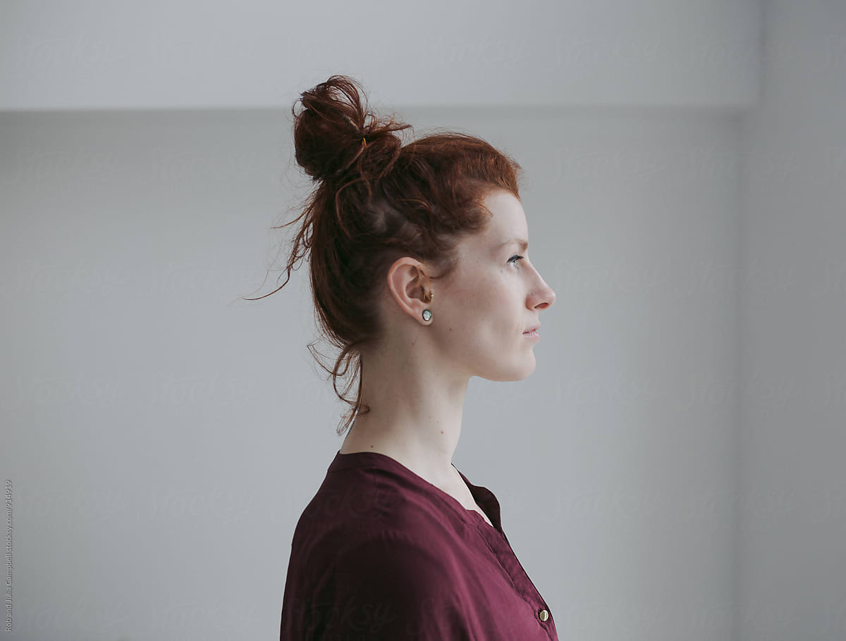 Serious profile portrait of red head woman on simple white background