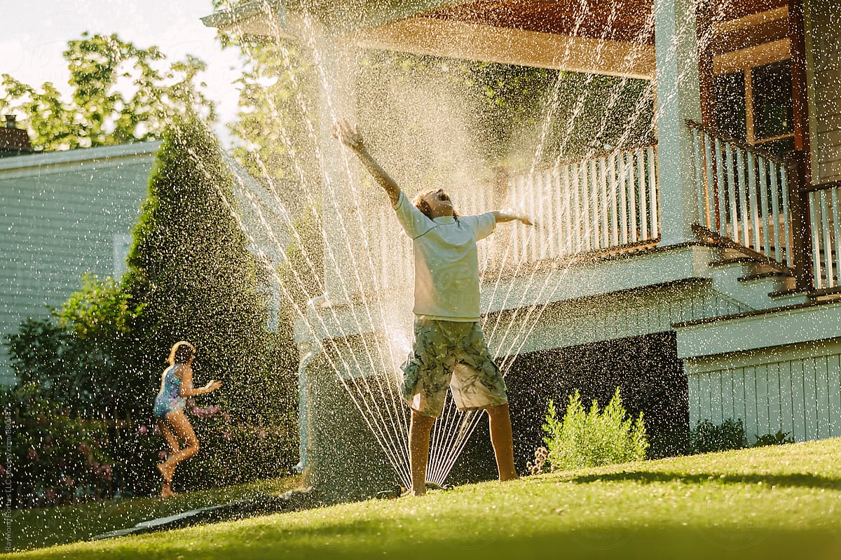 Happy Child Playing in Backyard Water Sprinkler