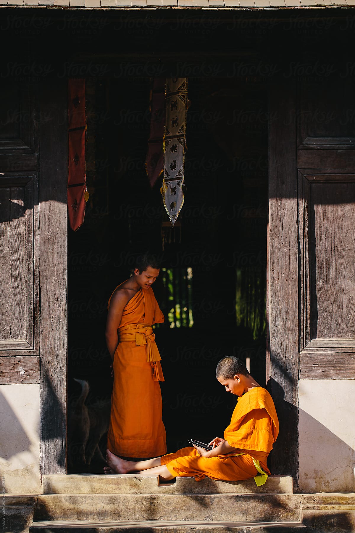 Two young Buddhist monks spending leisure time at the temple entrance