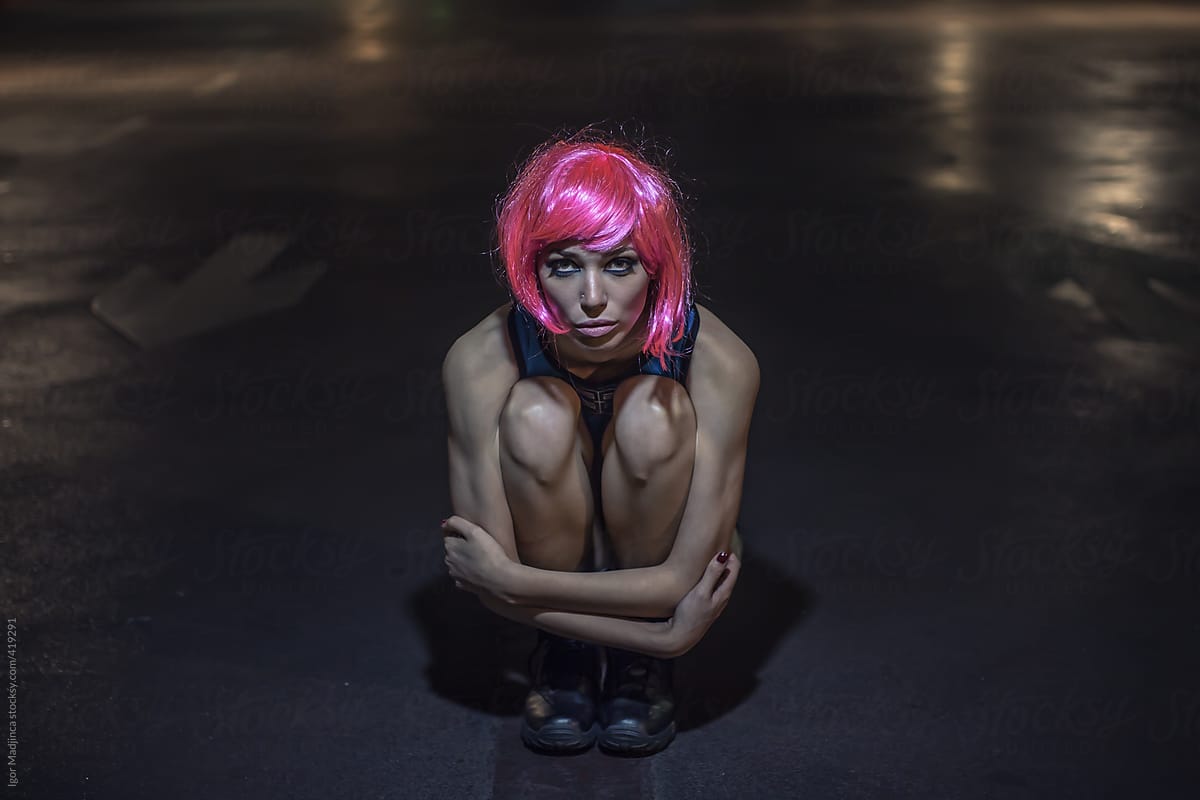 girl with a pink wig squatting on a parking lot