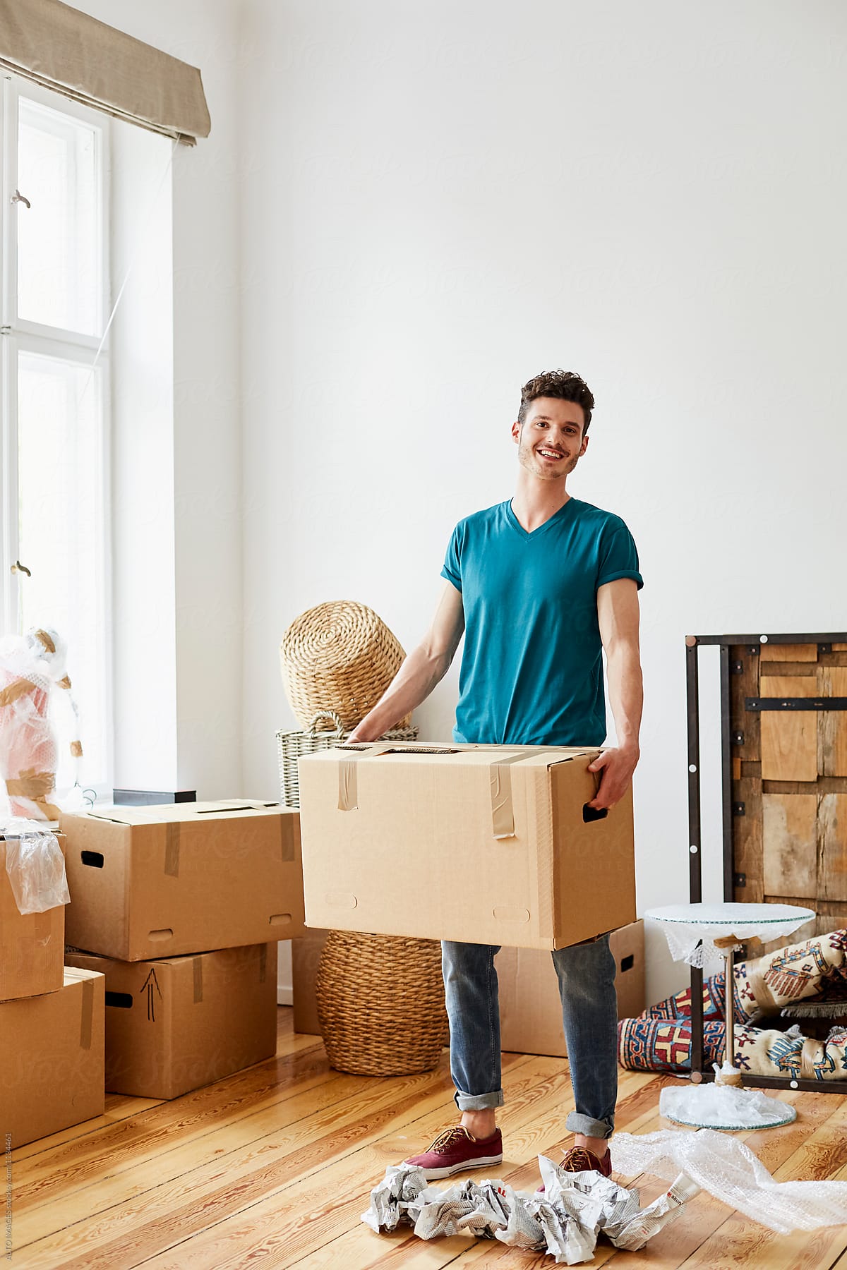 Happy Young Man Carrying Cardboard Box In New Apartment