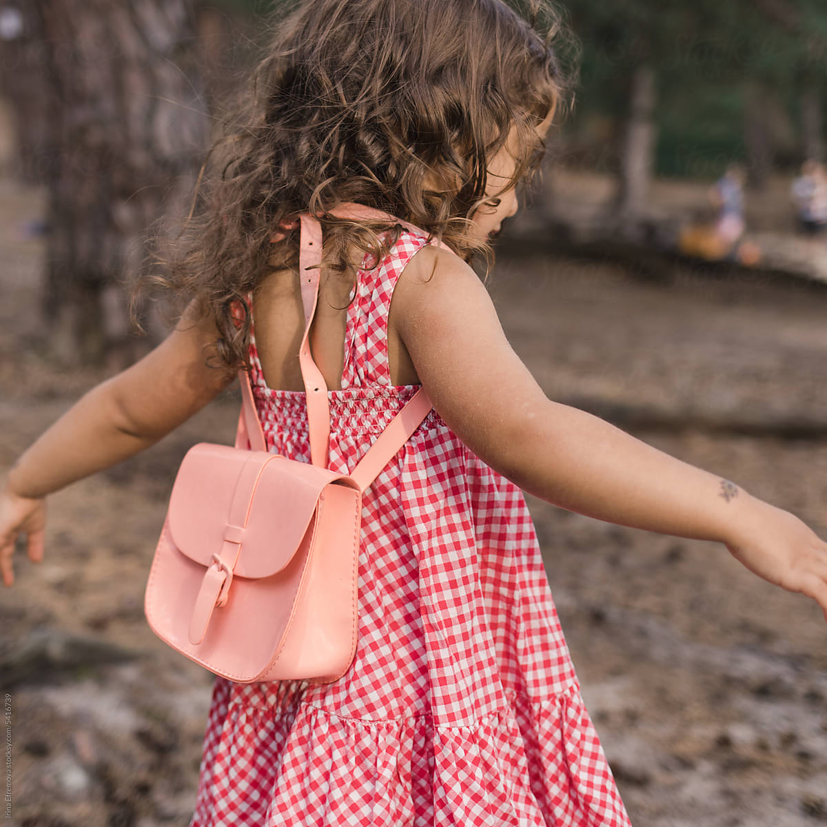 Dancing Little Girl in Red Dress with Pink Backpack seen from back