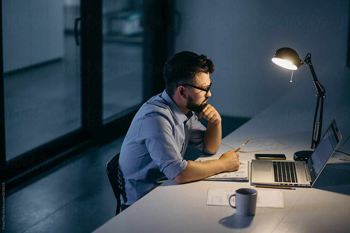Man sitting alone in the dark office in front of laptop and working  at night