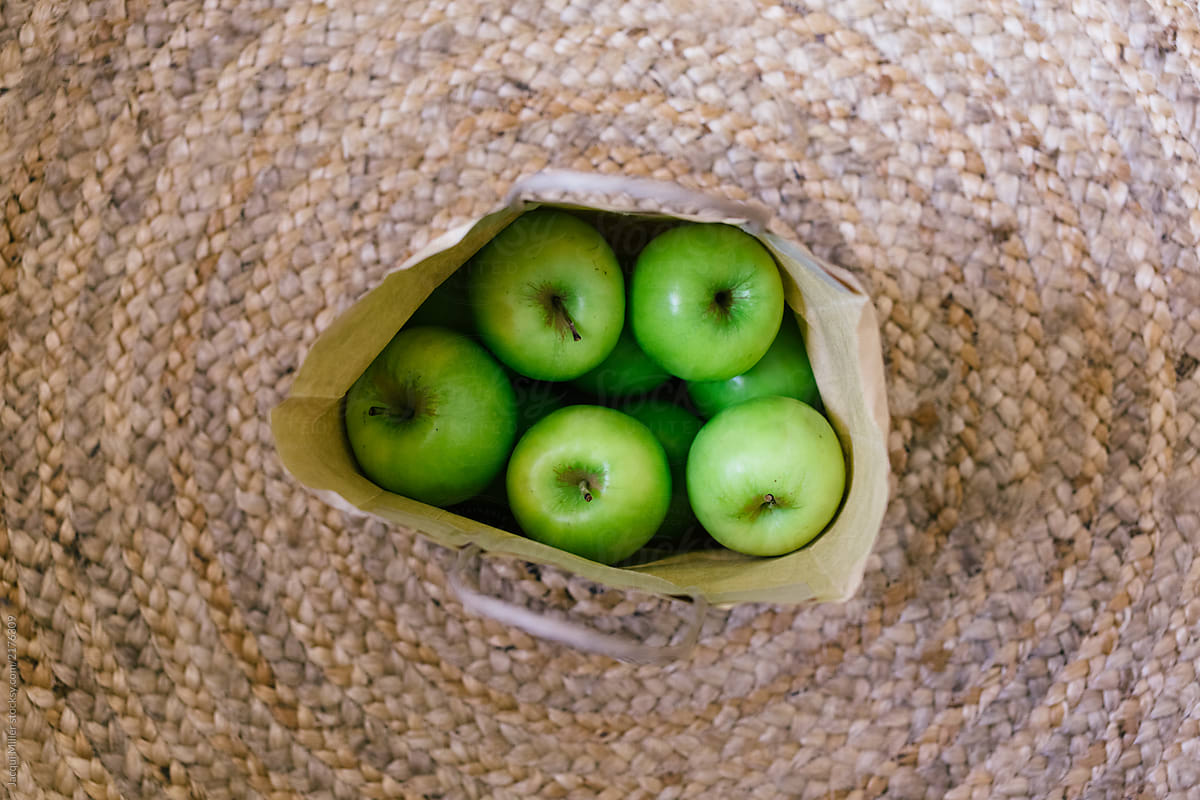 Paper bag of green apples on jute rug, from above