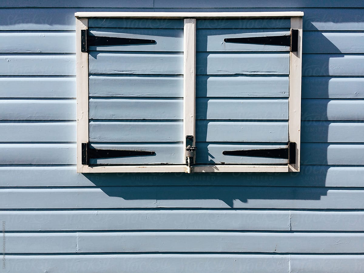 Window shutters on a blue wooden panelled beach hut. Norfolk, UK.