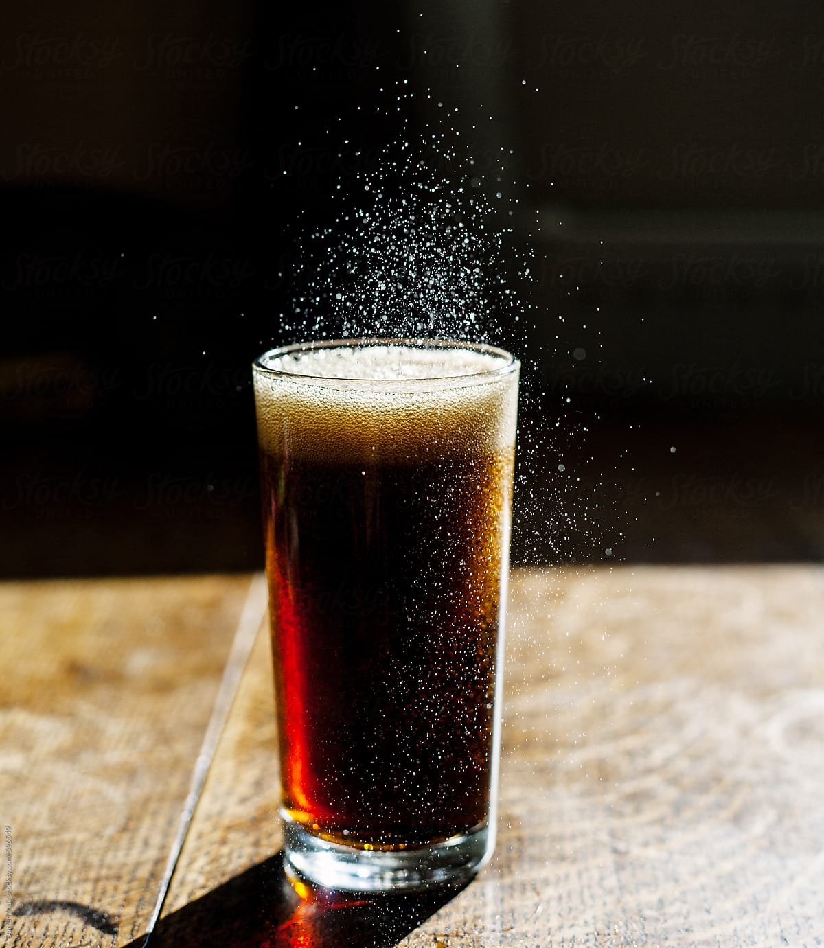 Fizzing glass of cola on wooden table.