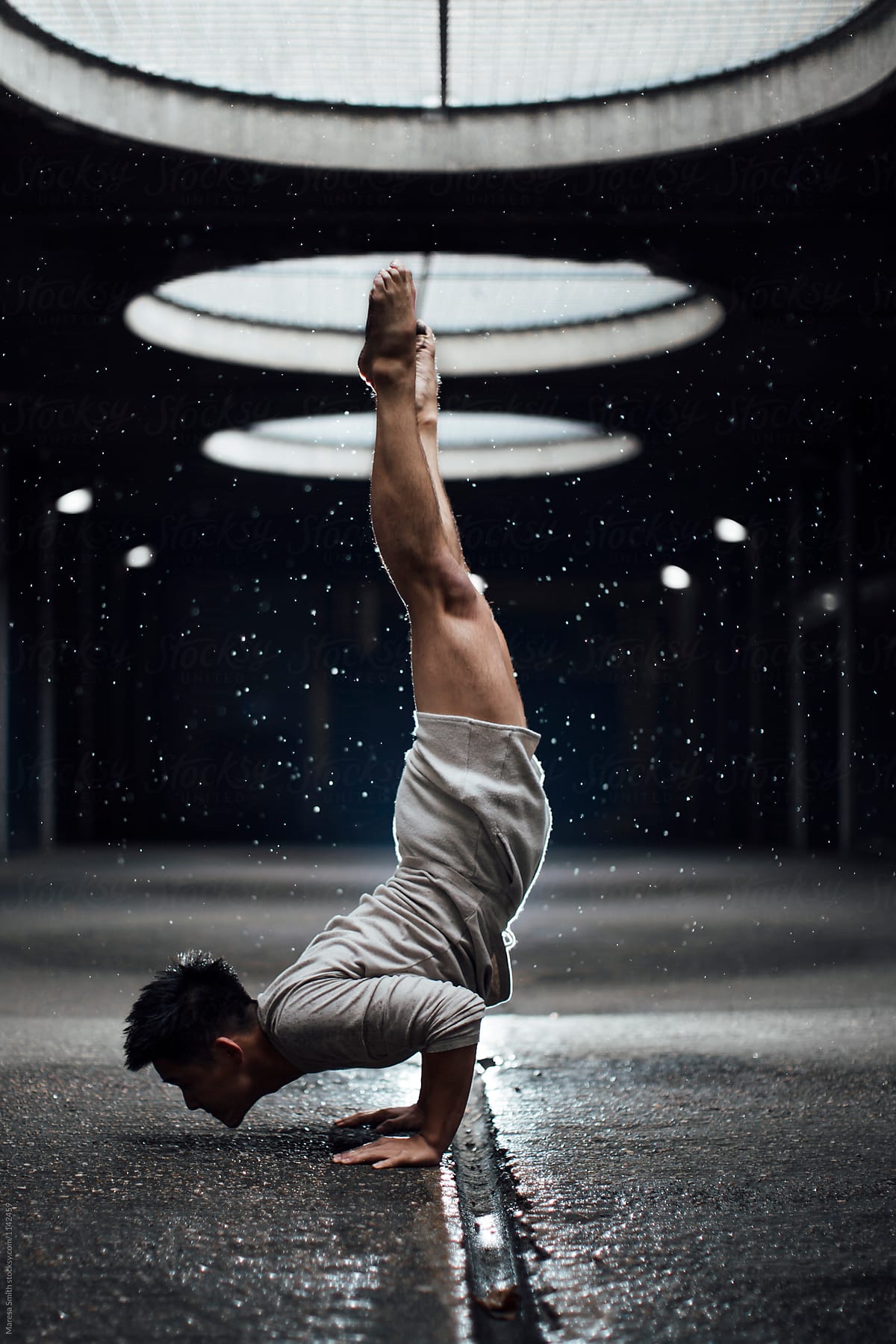 A male dancer and yoga artist practises a chinstand in an urban setting
