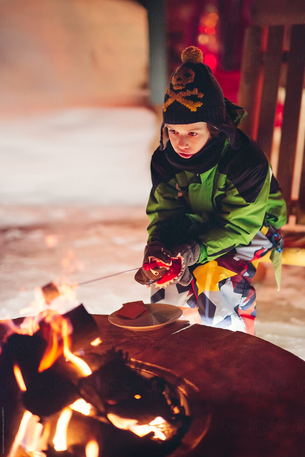 Boy toasting marshmallows over a camp fire at night surrounded by snow in winter
