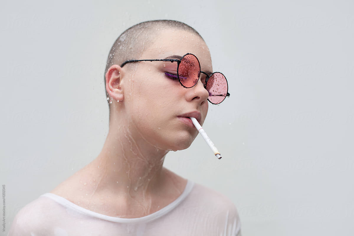 Bald woman with cigarette under water drops