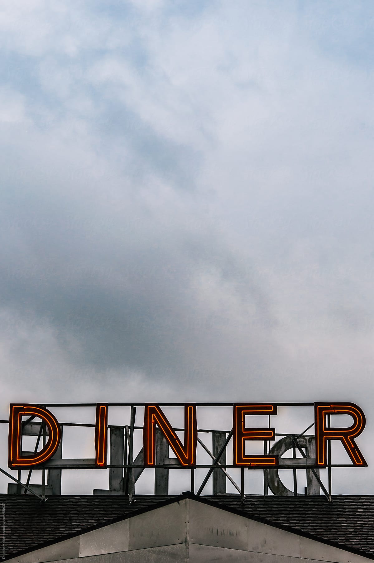 Red neon diner sign on a roof against clouds