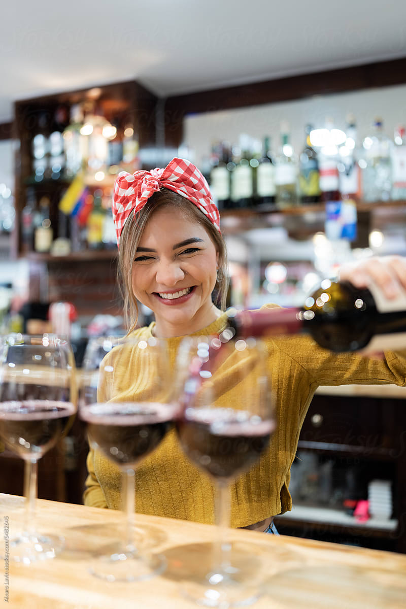 Woman serving red wine in glasses.