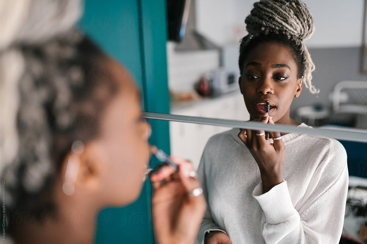 African American lady applying lipstick near mirror