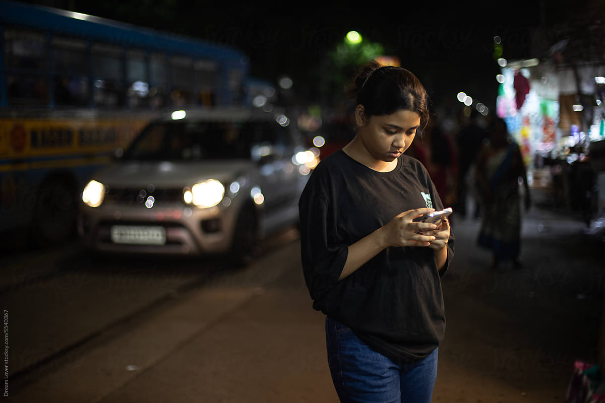 Young girl browsing smartphone in beside a busy street in Kolkata