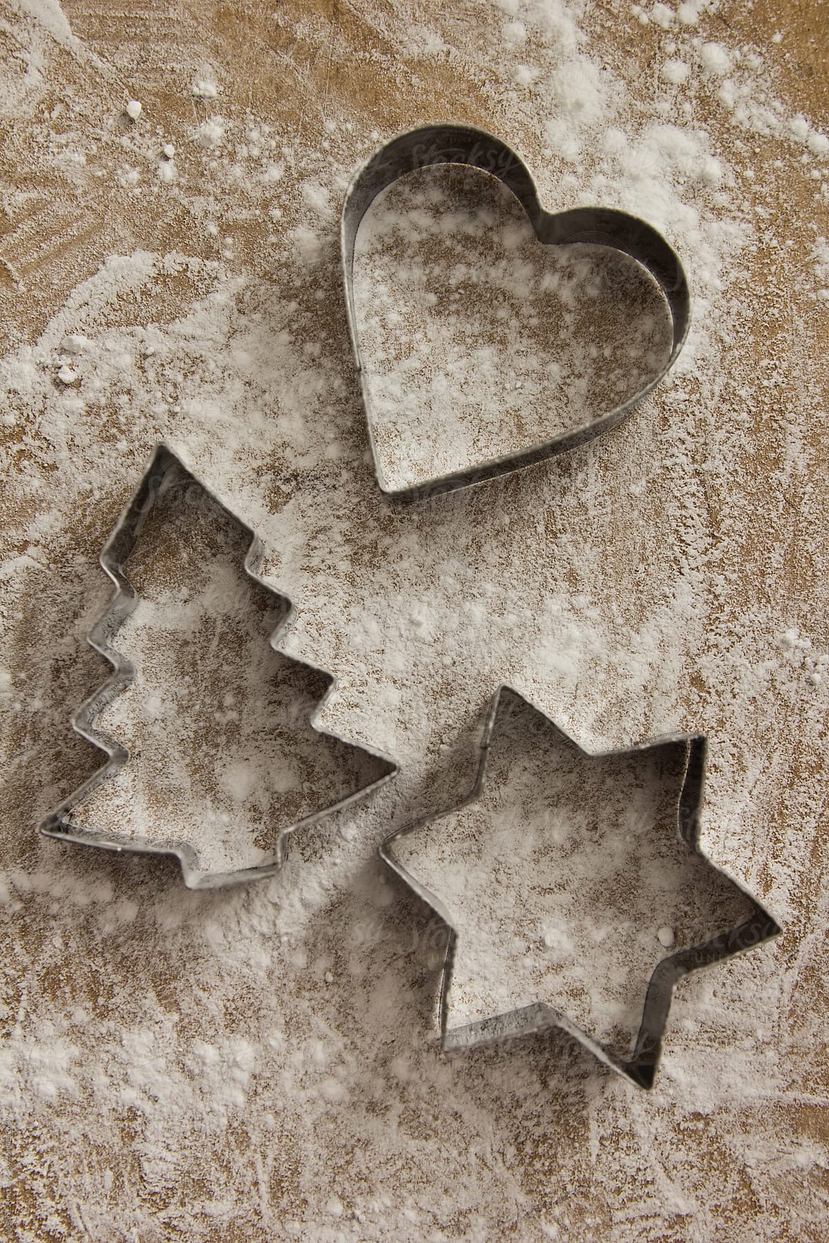 Star, heart and christmas tree shaped cookie cutters on wooden board covered with flour