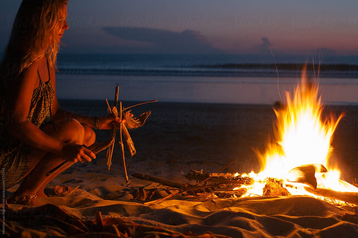 Girl makes a fire of driftwood on the beach with sunset