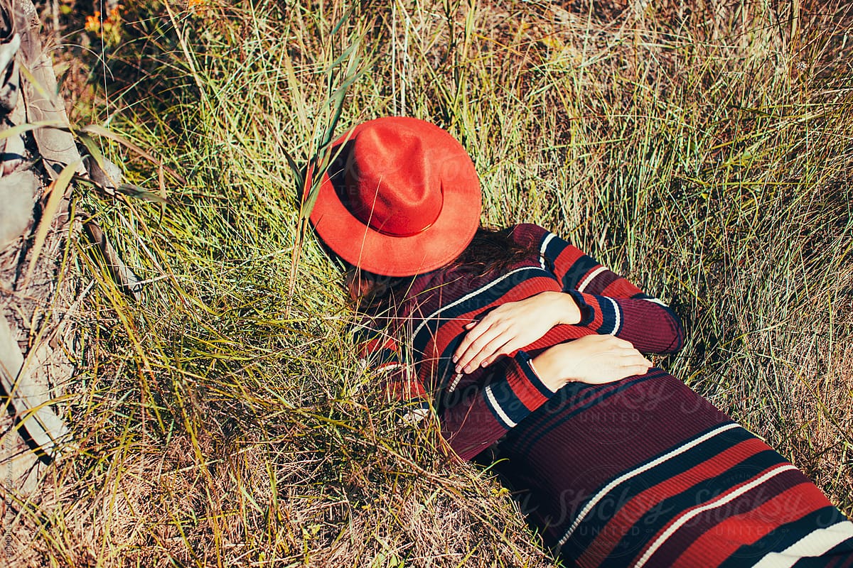 Anonymous Woman Hiding Her Face With A Hat Lying On The Grass By Stocksy Contributor