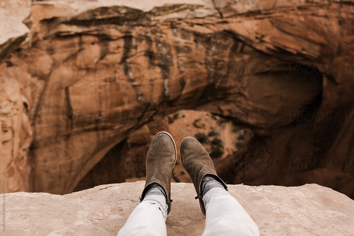 view of feet from sitting on edge of cliff in rocky desert landscape