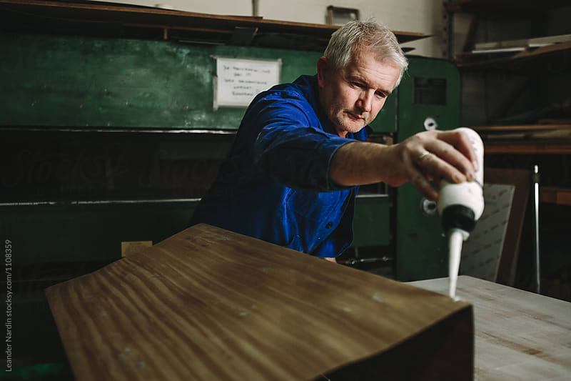 portrait of male senior woodworker applying glue on wooden veneer