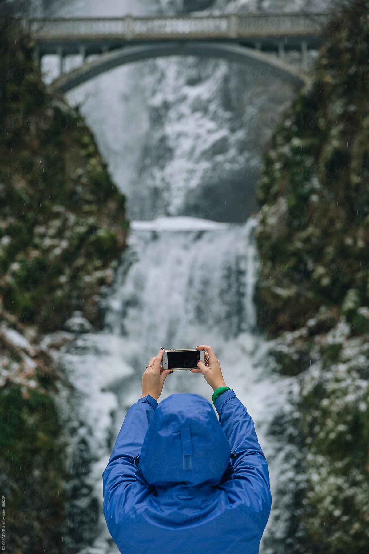 Woman taking a picture of a waterfall in winter.