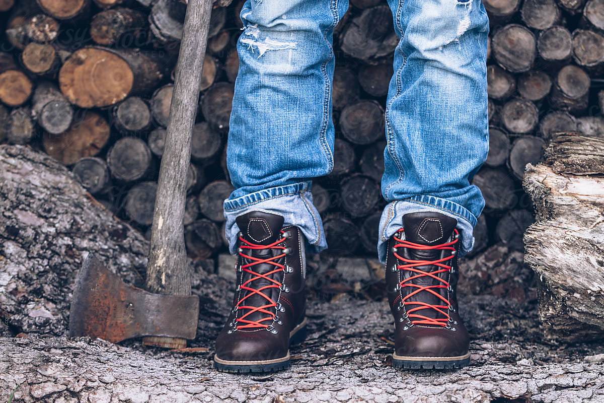 male legs in jeans and mountaineering boots on wooden background with an axe