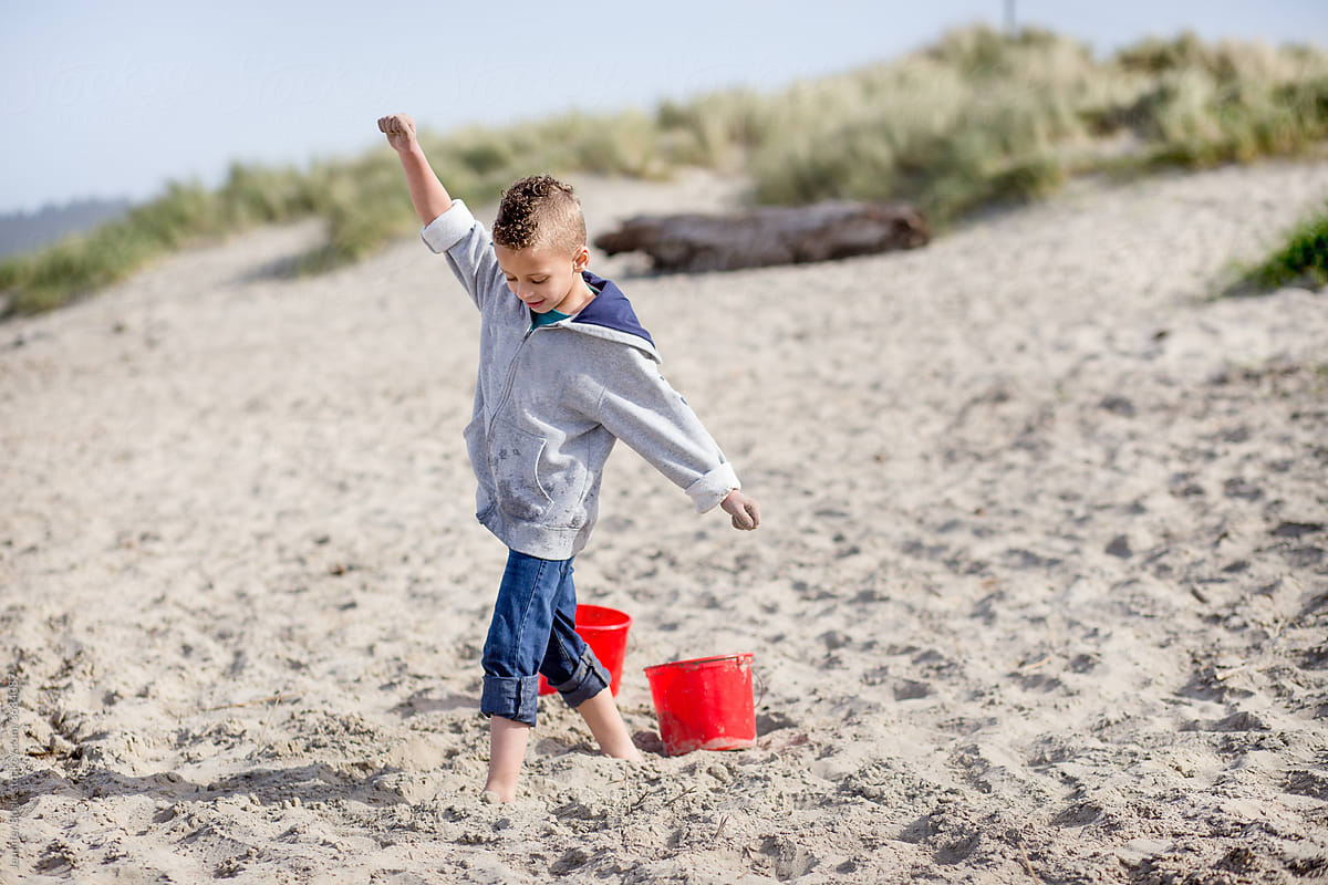 Energetic boy on sandy beach with bucket