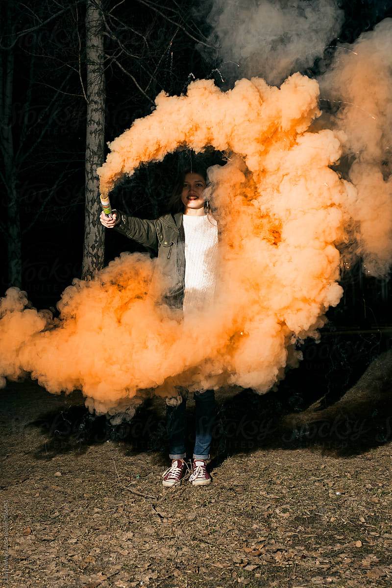 Portrait of young woman with orange smoke bomb