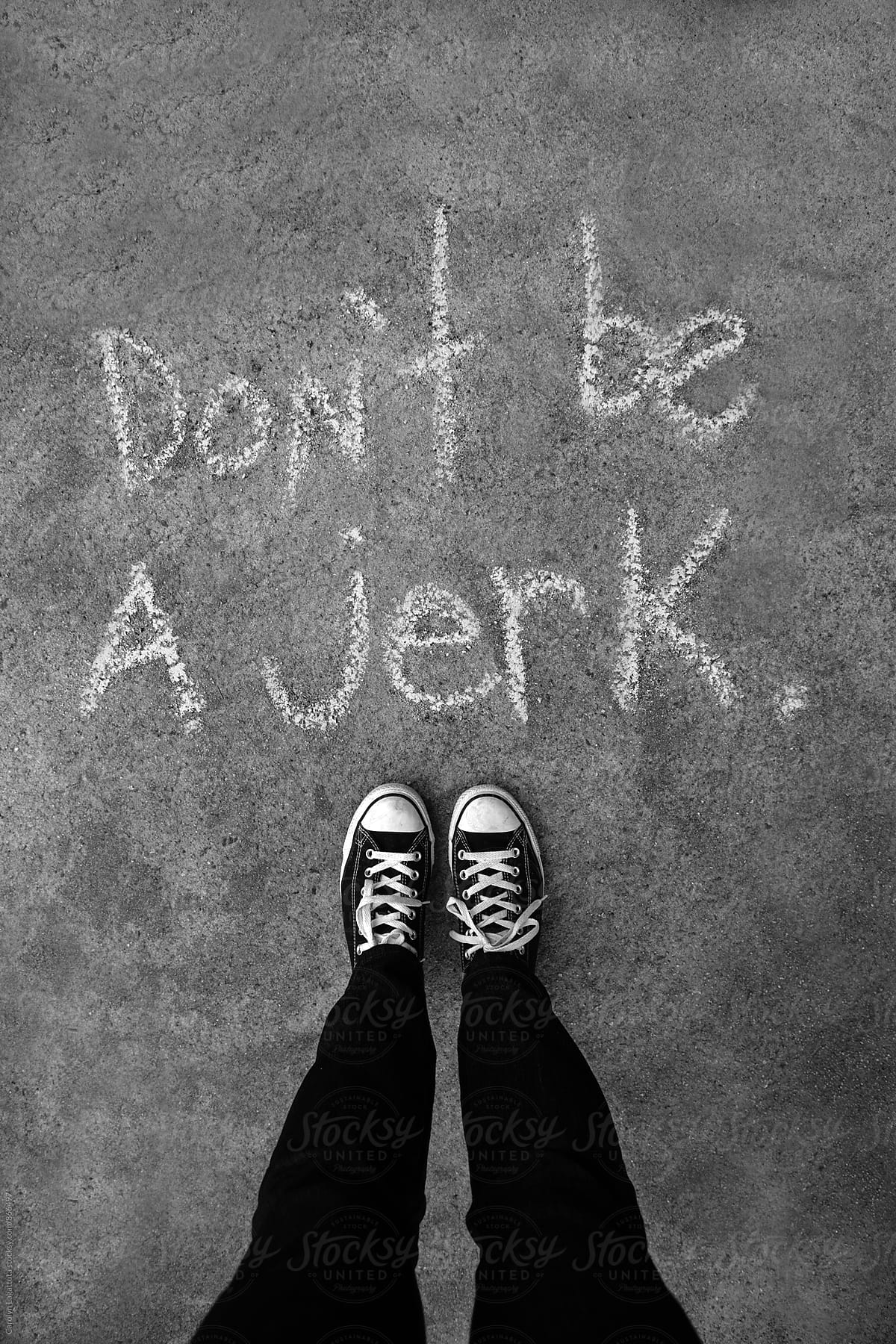 Person in black sneakers standing above chalk words saying - Don't be a jerk by Carolyn Lagattuta for Stocksy United