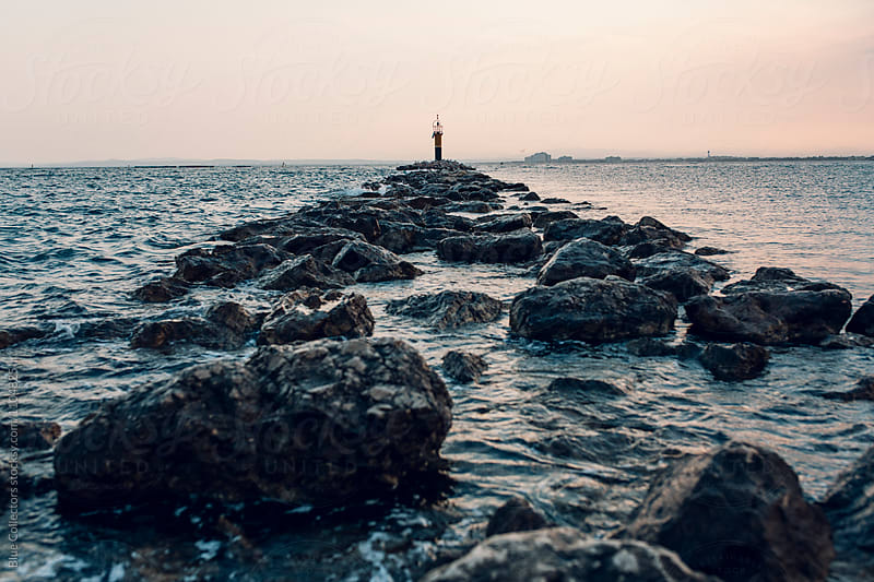 A lighthouse at sunset surrounded by water and rocky path, on focus