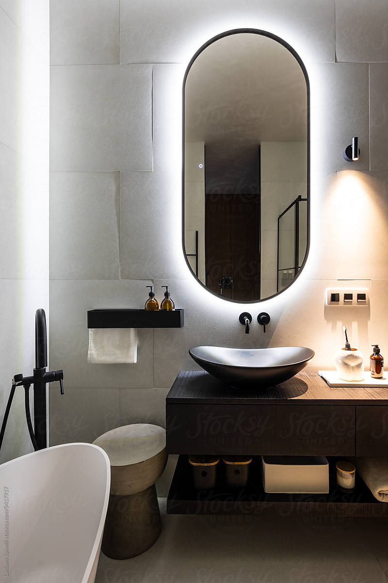 Bathroom with back lighted rounded mirror, bath and toiletry